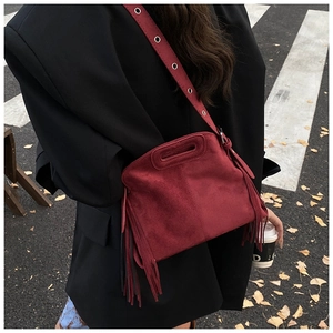 Detail of burgundy suede crossbody bag with long fringes and metal eyelets on strap