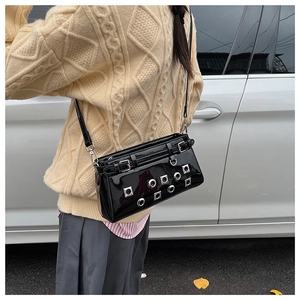 Detail of black patent leather crossbody bag with silver eyelets and punk rivets on a model