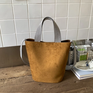 Detail of brown suede bucket bag featuring woven herringbone handle on a wooden table