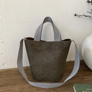 Detail view of vintage dark suede bucket bag with woven herringbone strap on wooden table