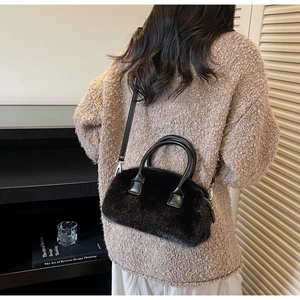 Detail of black faux fur handbag with leather straps worn crossbody in a cozy studio