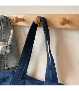 Detail of a dark blue denim tote bag hanging with wide shoulder strap and visible stitching