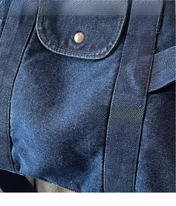 Detail of dark blue denim tote bag with silver button and neat stitching