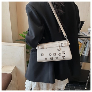 Detail view of cream punk style crossbody bag with metal rivets on black blazer