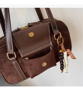 Detail of brown suede Boston bag with gold hardware, beaded tassel, and contrast stitching