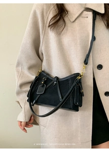 Detail of black suede crossbody bag with contrast stitching and gold-tone hardware