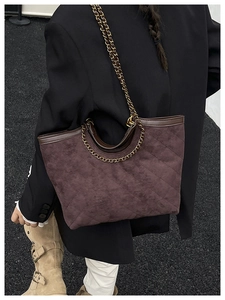 Detail of dark brown quilted suede tote bag with metal chain strap on female model