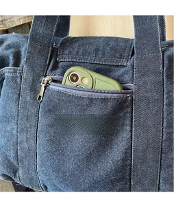 Detail of blue denim tote bag showing functional front zipper pocket and durable texture