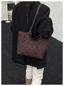 Detail of dark brown suede tote bag featuring diamond quilted stitching and chain strap