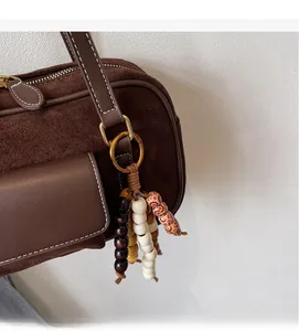 Detail of dark brown suede Boston bag with smooth leather pocket and wooden bead charm