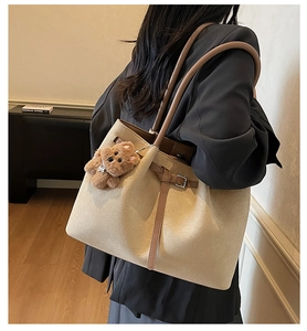 Detail view of large sand suede tote bag with brown leather straps and plush bear charm