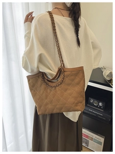 Detailed view of caramel brown quilted tote bag with metal chain strap on model