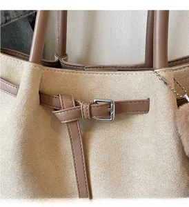 Close-up of beige suede tote bag showing silver metal buckle and brown leather strap