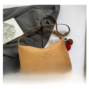 Detailansicht einer kamelfarbenen Wildleder-Halbmondtasche mit zweifarbigem Pompon-Anhänger