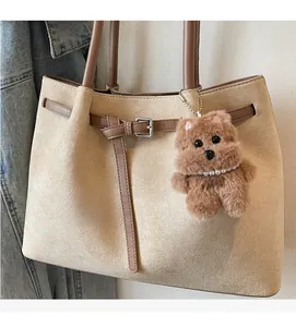 Detail of beige suede tote bag featuring brown strap buckle and plush bear charm accent