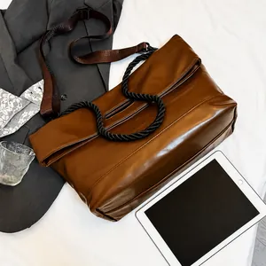 Detail of a brown matte leather tote with a black braided rope handle and wide shoulder strap