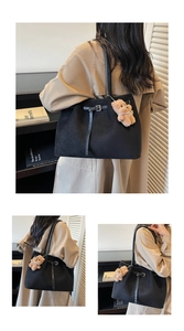 Detail of black tote bag with strap buckle, plush bear charm, and suede texture
