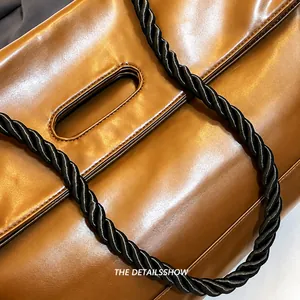 Macro detail of brown leather tote featuring a black braided rope strap and cutout handle