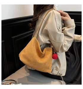 Close-up of mustard yellow suede tote bag showing soft texture and red pom-pom charm