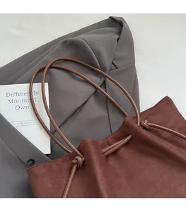 Detail of dark brown suede tote bag featuring slim round straps and drawstring closure