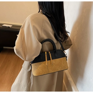 Detail of a quilted shell-shaped handbag with adjustable strap and dual zipper in two-tone leather