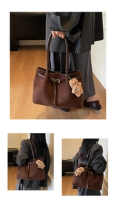 Detail of dark brown suede tote bag with leather strap buckle and plush bear pendant
