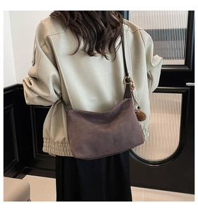 Brown suede dumpling shoulder bag featuring a fuzzy pom-pom charm and leather strap