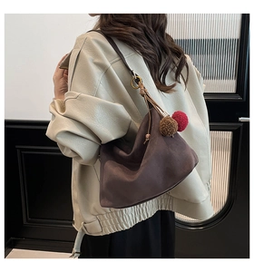 Close-up of brown suede hobo bag with long tassel knots and decorative pom-pom charms