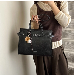 Detail of black matte leather tote bag with metal buckle and baseball glove charm accessory
