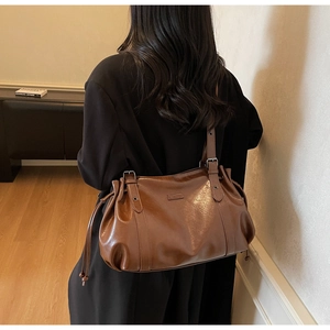Detail of vintage brown leather tote bag showing side drawstring and metal logo on strap