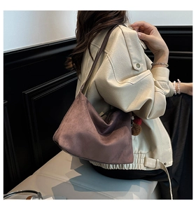Detail of suede shoulder bag in dark brown with tassel charm on street style model
