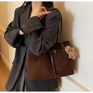 Details einer braunen Wildleder-Tragetasche mit Gürtelschnalle und Plüschbär am Modell