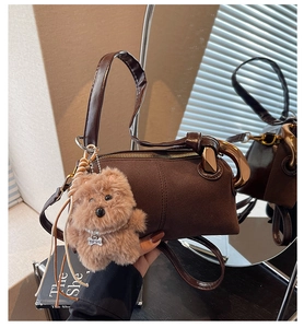 Detail of a brown cylindrical crossbody bag with a fuzzy teddy bear charm and gold ring