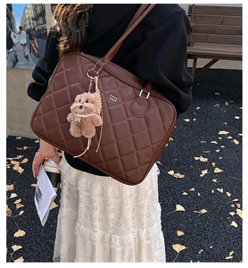 Close-up of quilted brown tote bag with metal logo and cute plush bear charm on strap