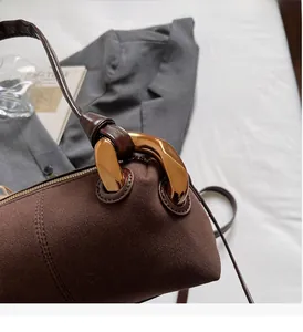 Detailed view of dark brown suede cylinder bag with bold gold metallic chain link