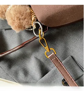 Detail of dark brown suede cylinder bag with gold hardware and plush bear charm