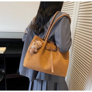 Brown suede tote bag with leather straps and bear charm shown on model in urban style