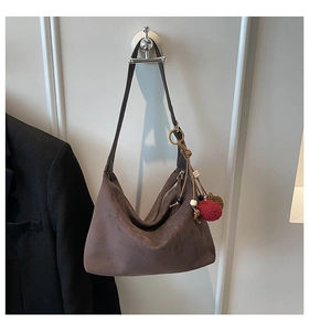 Detail of dark brown suede hobo bag featuring a decorative red pompom and wooden beads charm