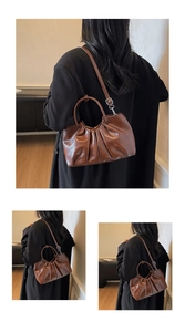 Borsa a mano in ecopelle plissettata marrone scuro indossata su un cappotto nero elegante