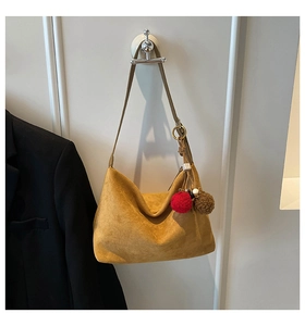 Close-up of mustard yellow suede hobo bag featuring decorative plush ball charms
