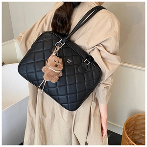 Close-up of quilted black leather tote bag with a brown plush bear charm and pearls