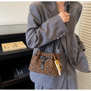 Detail of leopard print bucket bag with beaded charm and black leather handle straps