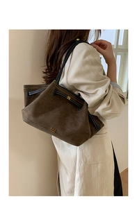 Close-up of brown suede bucket bag featuring gold brand logo and black leather drawstring