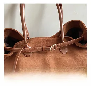Detailed close-up of premium metal hardware and stitching on a dark brown suede tote bag