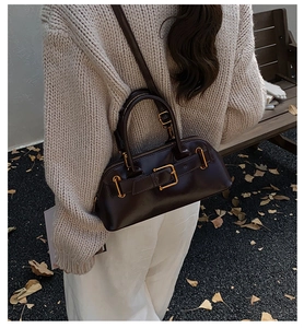 Detail of dark brown leather shell bag featuring gold buckle and dual zipper design