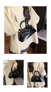Detailed view of black patent leather shell bag with golden metal buckle and zipper