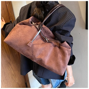 Detail of a large brown suede tote bag with leather straps on a model in a blazer