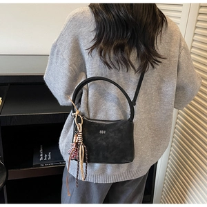 Detail of black matte leather bucket bag featuring a sturdy handle and woven charm accessory
