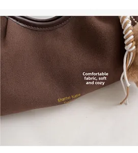 Dettaglio borsa scamosciata marrone con logo dorato e ciondolo decorativo a pompon
