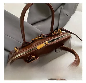 Detailed close-up of the golden zipper and metal D-ring on the brown leather shell bag